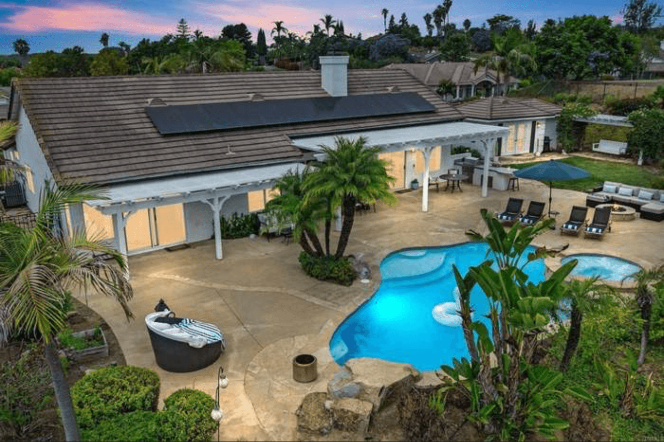 Backyard with a blue swimming pool, patio furniture, palm trees, and rooftop solar panels.