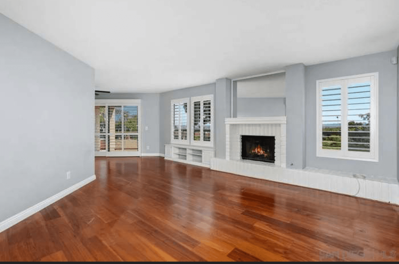 Spacious living room with hardwood floors, a white brick fireplace, and large shuttered windows.
