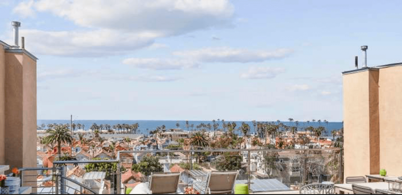 Rooftop view overlooking a coastal town with palm trees and the blue ocean horizon.
