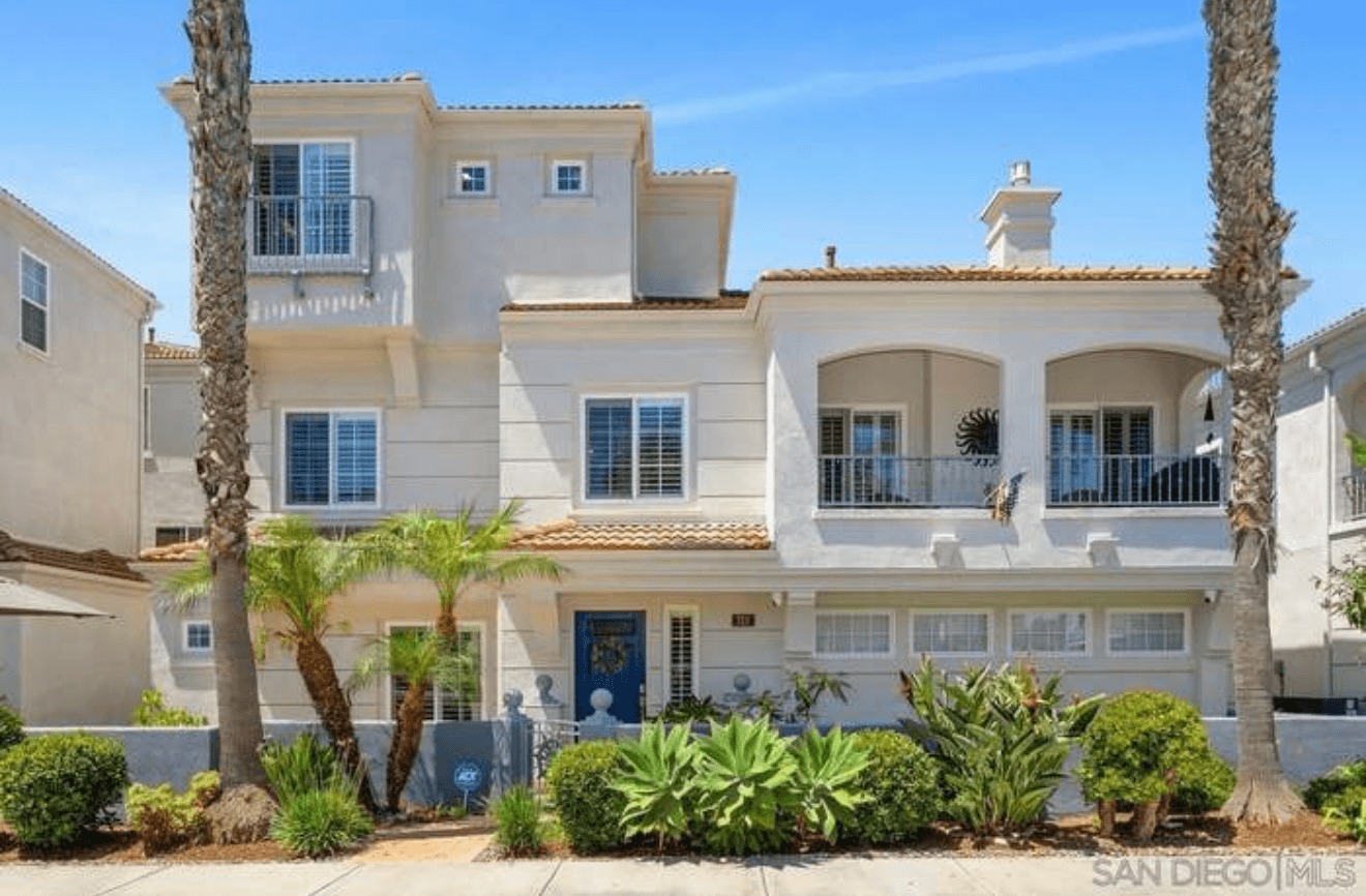 Modern three-story white house featuring balconies, a blue front door, and lush tropical landscaping.