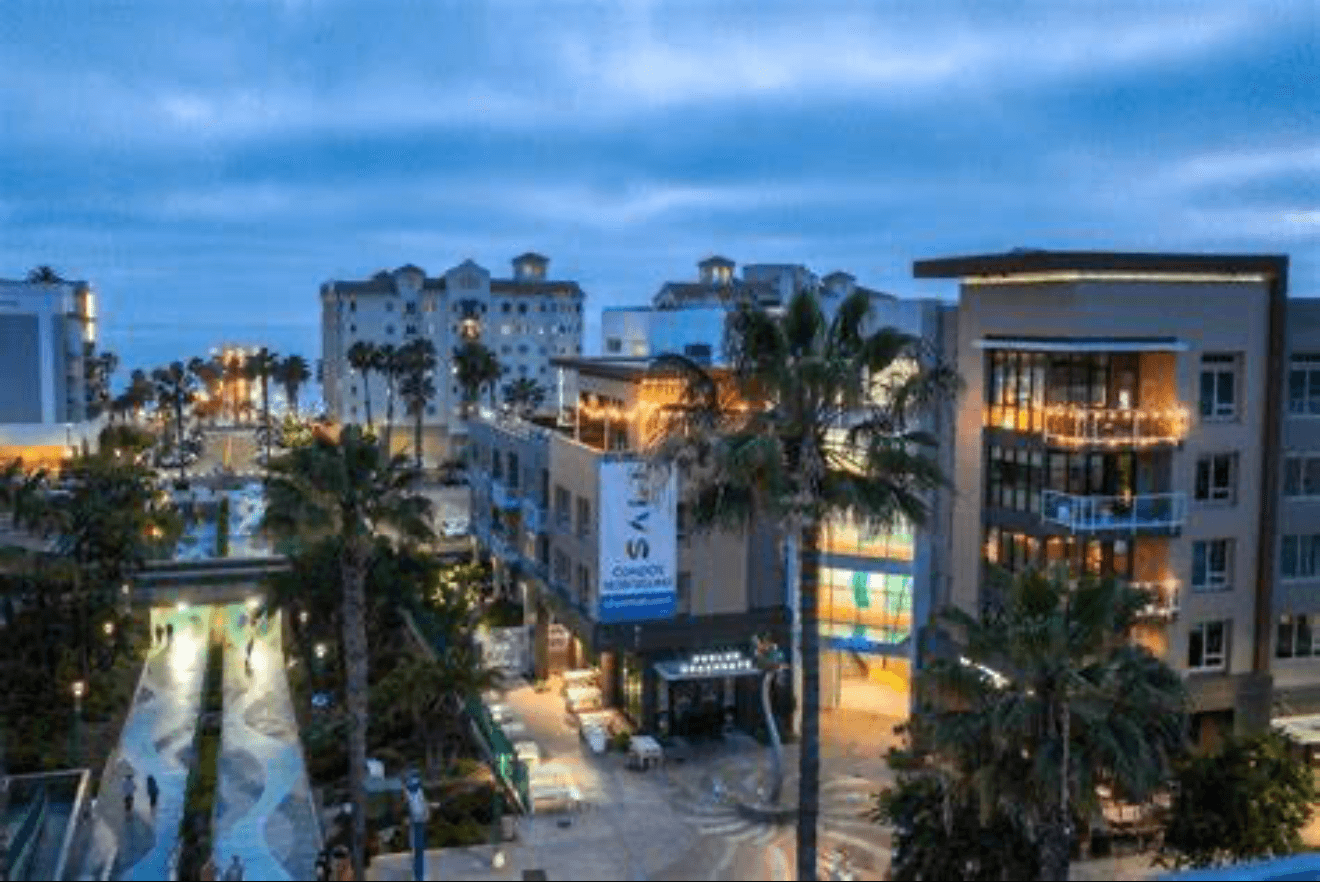 Modern beachfront buildings and palm trees at dusk with a patterned walkway and ocean view.